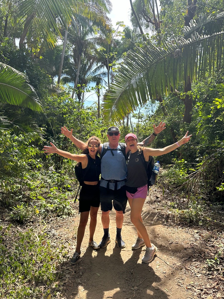 Three hikers with arms raised on a jungle trail