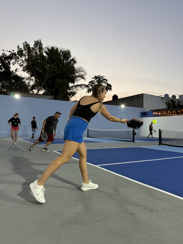 Woman lunging into a forehand at dusk on the Nawalli court