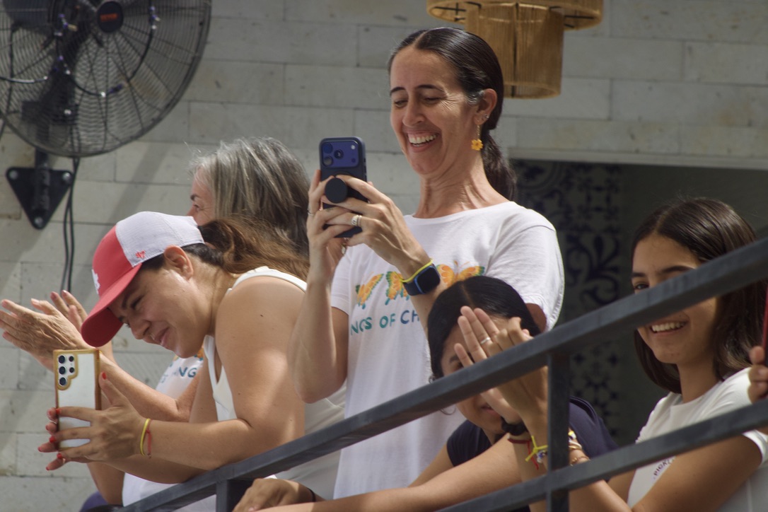 Spectators laughing and filming from the balcony above the courts